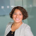 A confident woman with curly hair smiling in an office environment, conveying professionalism and approachability.