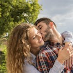 Happy couple sharing a loving embrace outdoors with a scenic background.